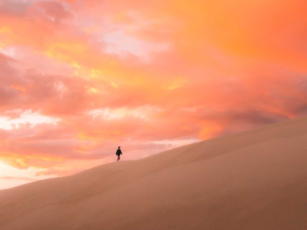 Wandelaar alleen op zandheuvel onder rode lucht